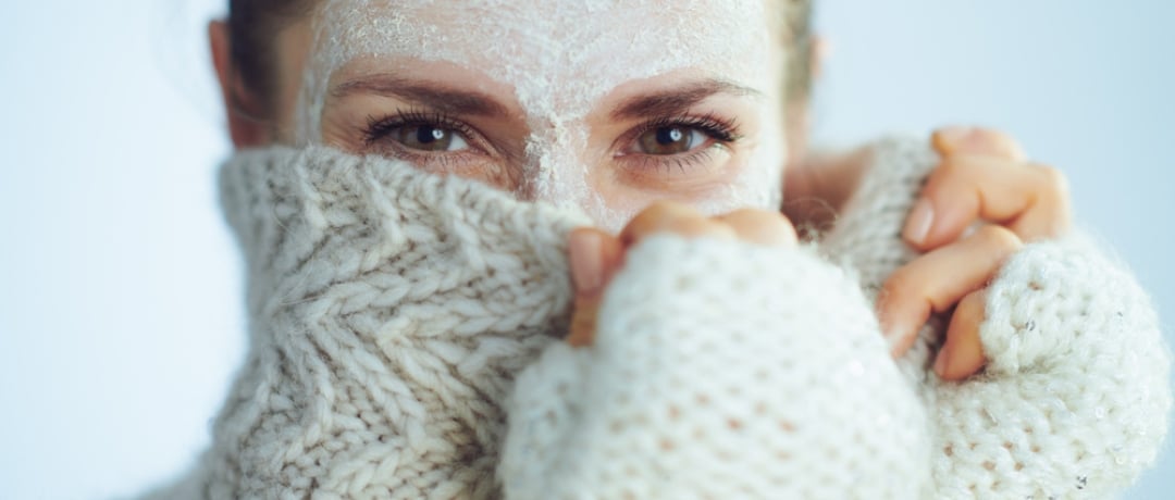 Elegant woman in roll neck sweater and cardigan with white facial mask hiding behind clothes